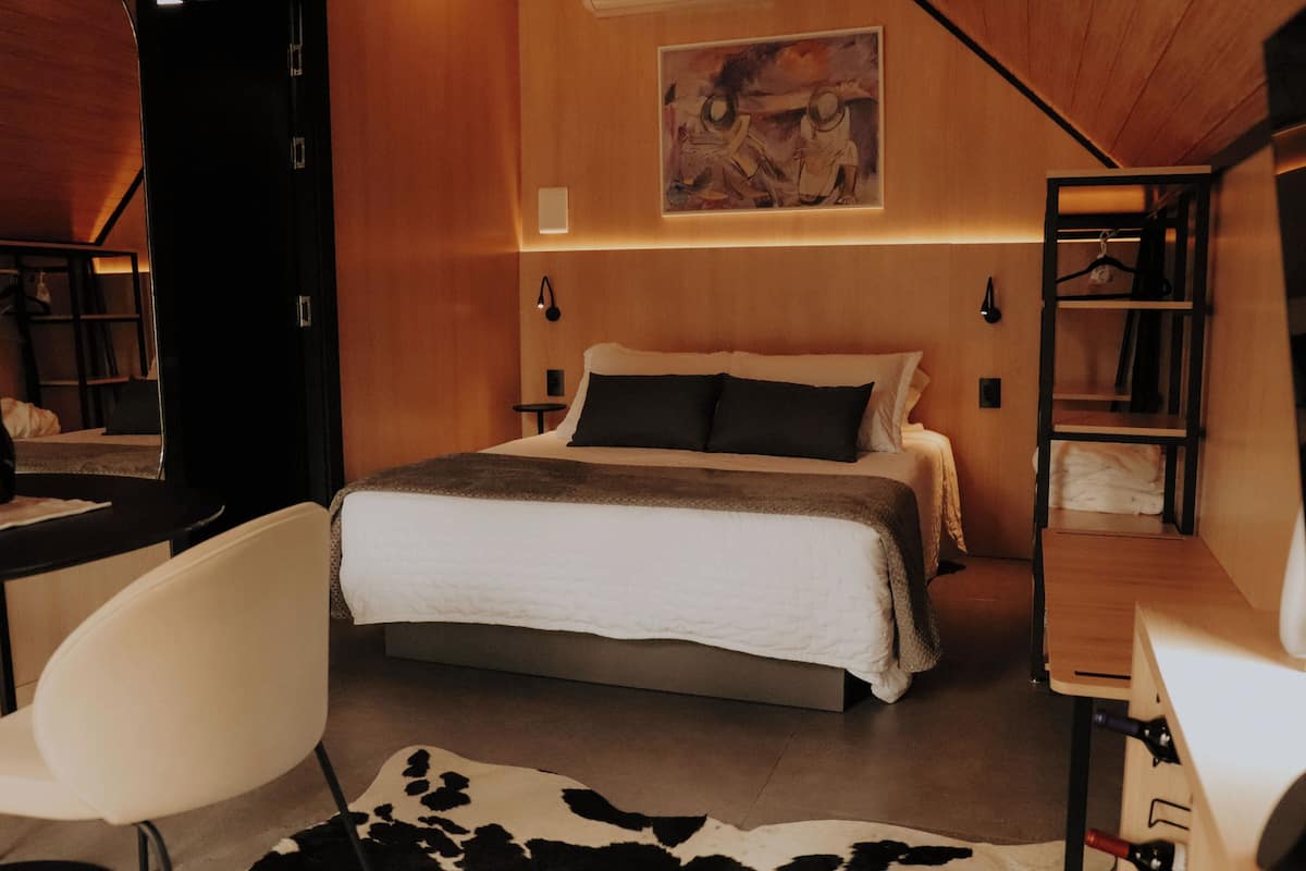 A modern hotel room with a bed, a desk, a chair, and a coat rack.