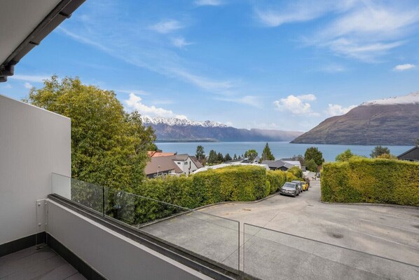 A balcony with a view of a lake, mountains, and a parking area with cars. - Fernhill Falls Retreat | Lake Views & Parking (Queenstown)