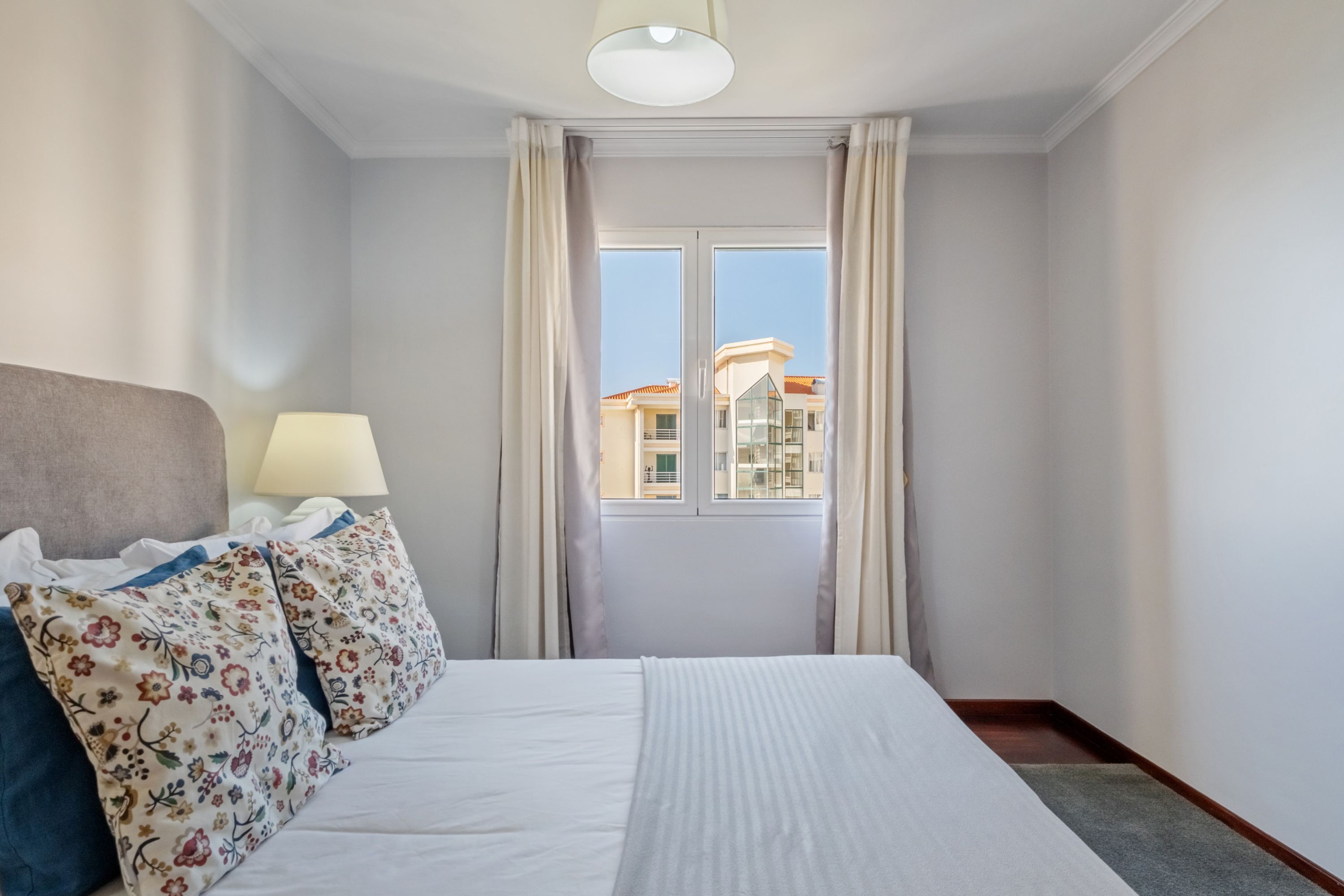 Habitación de hotel con cama, lámpara y vista a edificios a través de una ventana.