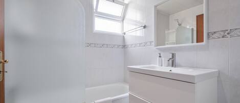A modern bathroom with a bathtub, a vanity with a mirror, and a window.