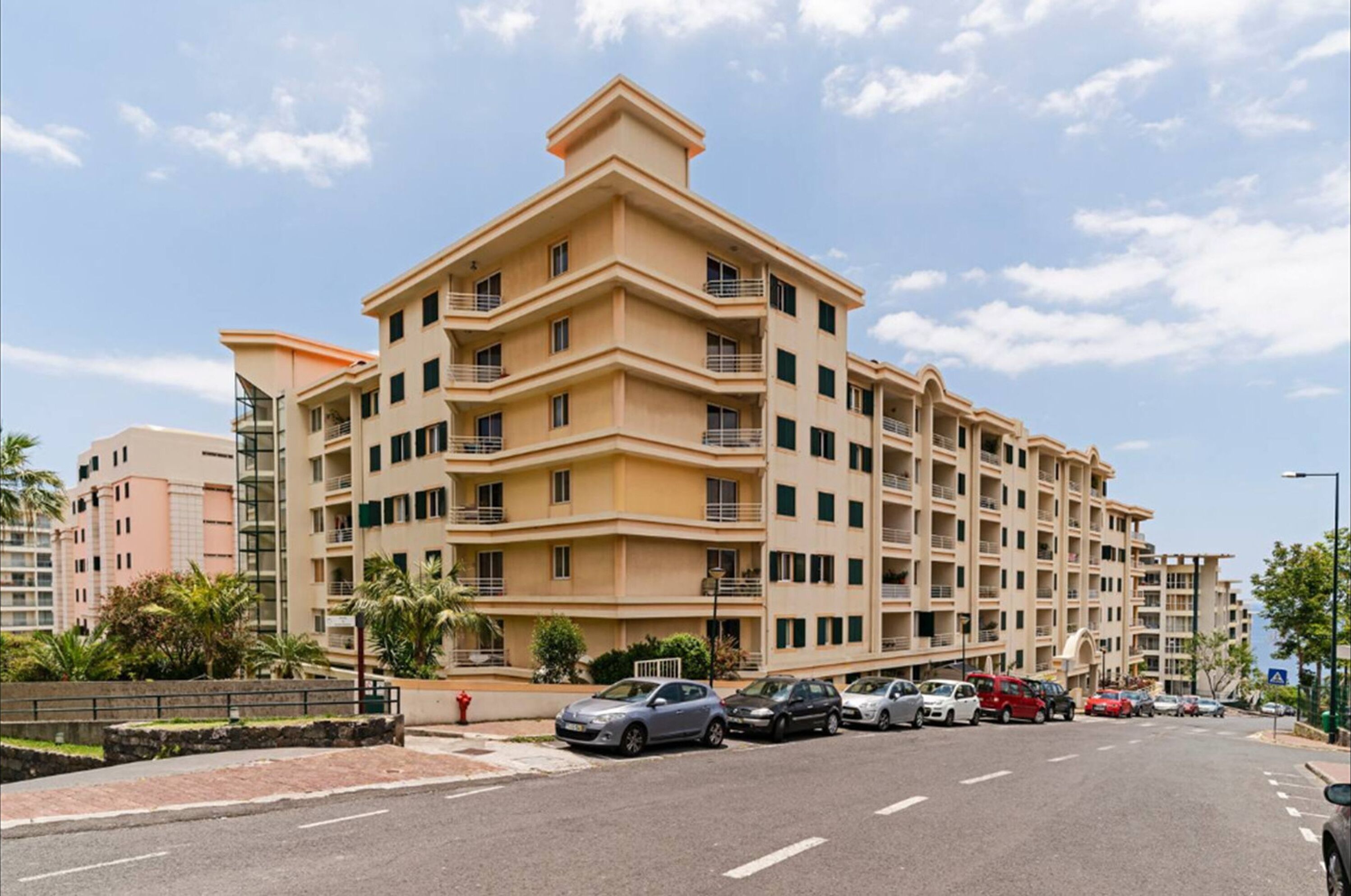 A multi-story residential building with balconies, a parking lot, and a clear sky.