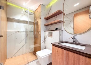 A modern bathroom with a glass-enclosed shower, a wooden vanity, and marble walls. - JVC Sleeps 4 With Private Balcony (Dubai)