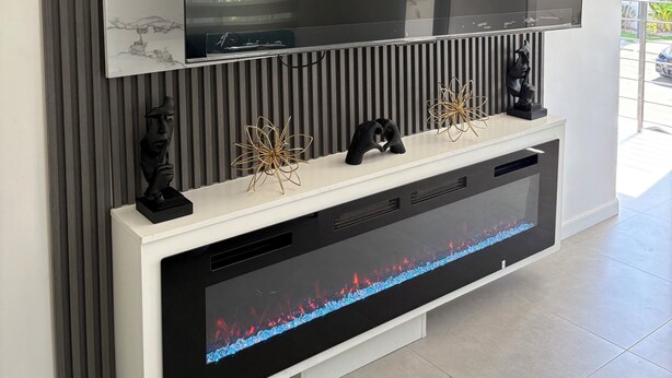Ein modernes Wohnzimmer mit einem großen Flachbildfernseher, der an einer Wand mit marmorähnlichem Design angebracht ist. Darunter befindet sich eine schwarze Unterhaltungsecke mit integriertem Kamin.