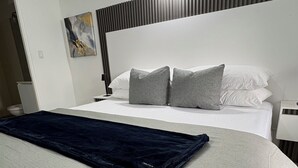 A modern hotel room with a neatly made bed, a dark blue blanket, and a wall-mounted light fixture.