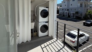 Ein Balkon mit Waschmaschine, Ventilator und Blick auf eine Straße und Gebäude.