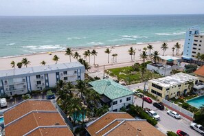Un hotel frente al mar con varias construcciones, una piscina y una playa con palmeras.