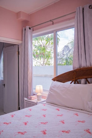 Quarto com cama, mesa de cabeceira, abajur e janela com cortinas.