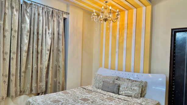 A bedroom with a bed, curtains, a chandelier, and a striped wall.