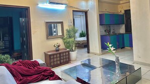 A living room with a glass coffee table, a red blanket, a wooden cabinet, and a potted plant.