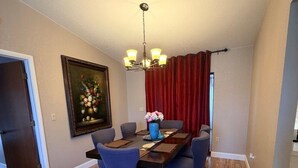 Een eetgedeelte met een houten tafel, blauwe stoelen, een kroonluchter en een rood gordijn.