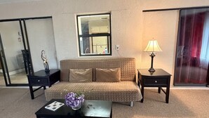 Een gemeubileerde woonkamer met een bank, twee bijzettafels, een salontafel met een bloevas, een lamp en een grote spiegel.