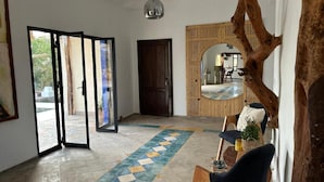 A spacious room with a tiled floor, a wooden door, a large mirror, and a rustic tree trunk decoration. - LaPerleD'argan (Essaouira)