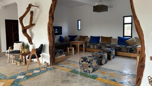 A modern living room with a large sectional sofa, a coffee table, and a unique wooden tree sculpture. - LaPerleD'argan (Essaouira)