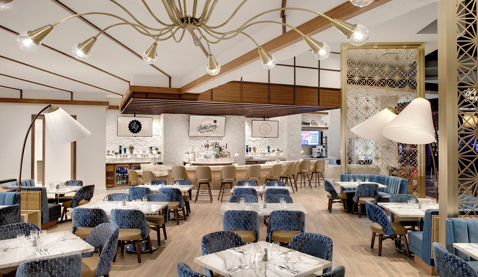 A restaurant with a modern interior, featuring blue upholstered chairs, white tables, and a bar area with a decorative wall.