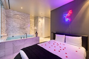 Een moderne hotelkamer met een marmeren badkamer, een bed met rozenblaadjes en een neonbord.