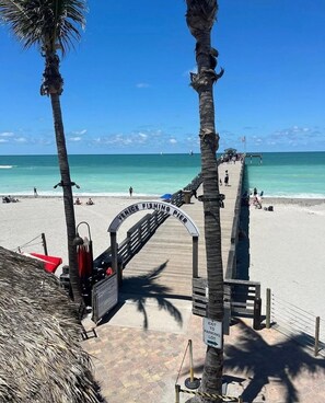 Una entrada a la playa con un letrero que dice 'Venice Fishing Pier' y un letrero que indica 'Salida al estacionamiento'.