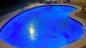 A swimming pool with a blue tint, surrounded by a tiled deck and a wooden fence.