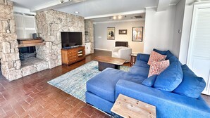 A living room with a stone fireplace, a blue sofa, and a television.