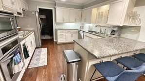 A kitchen with white cabinets, stainless steel appliances, a granite countertop, and blue bar stools.