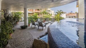 Zona de piscina exterior con un camino de piedra, sillas de descanso y plantas en macetas.
