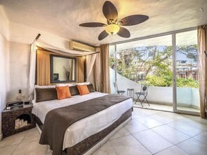 Un dormitorio con una cama grande, ventilador de techo, balcón con vistas y una pequeña mesa con sillas.