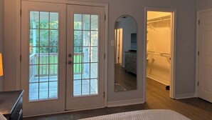 Et værelse med en stor skydedør, der fører til en terrasse, et walk-in closet og et spejl der reflekterer rummet.