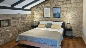 Een slaapkamer met een stenen muur, een houten bed, twee nachtkastjes met lampen en twee ingelijste foto's aan de muur.