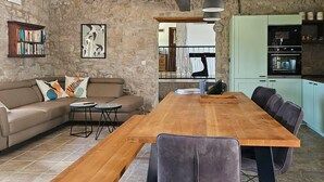 Een moderne woonkamer met een houten eettafel, een bank en een keukenhoek met lichtgroene kastjes.