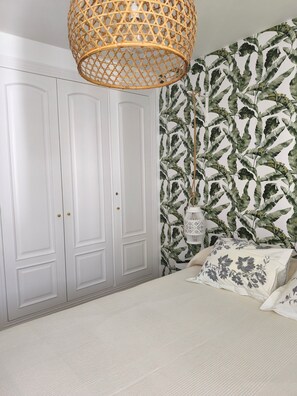 Een slaapkamer met een bed, een witte garderobe en een muur met een bladmotief.
