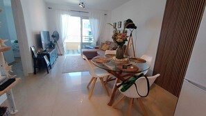 Een moderne woonkamer met een glazen eettafel, witte stoelen, een bank en een groot raam.
