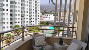 Un balcón con dos sillas, una mesita y vista a una piscina y edificios.