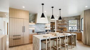Cozinha moderna com armários de madeira, bancada de mármore e iluminação pendente.