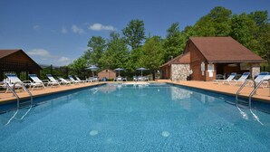 Ein rechteckiger Pool mit Liegestühlen und Sonnenschirmen, umgeben von Holzbauten und Bäumen.