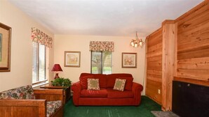 A cozy living room with a red sofa, wooden walls, and a green carpet. - Deluxe 1BR w/ Patio | Golf Nearby + Resort Pools (Champion)