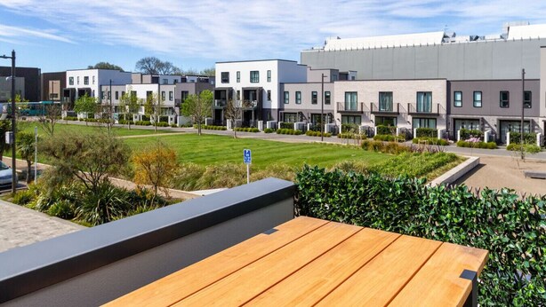 A modern residential area with multi-story buildings, a grassy courtyard, and a wooden deck.