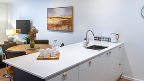 Una cocina moderna con encimera blanca, un fregadero y una zona de comedor con mesa y sillas.