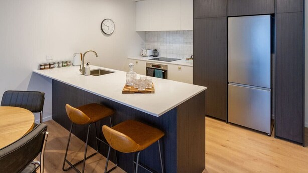 Una cocina moderna con una isla central, taburetes de bar, un refrigerador y un reloj en la pared.