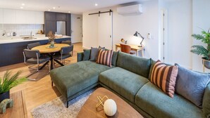 Una sala moderna con un sofá modular, una mesa de comedor y una cocina al fondo.