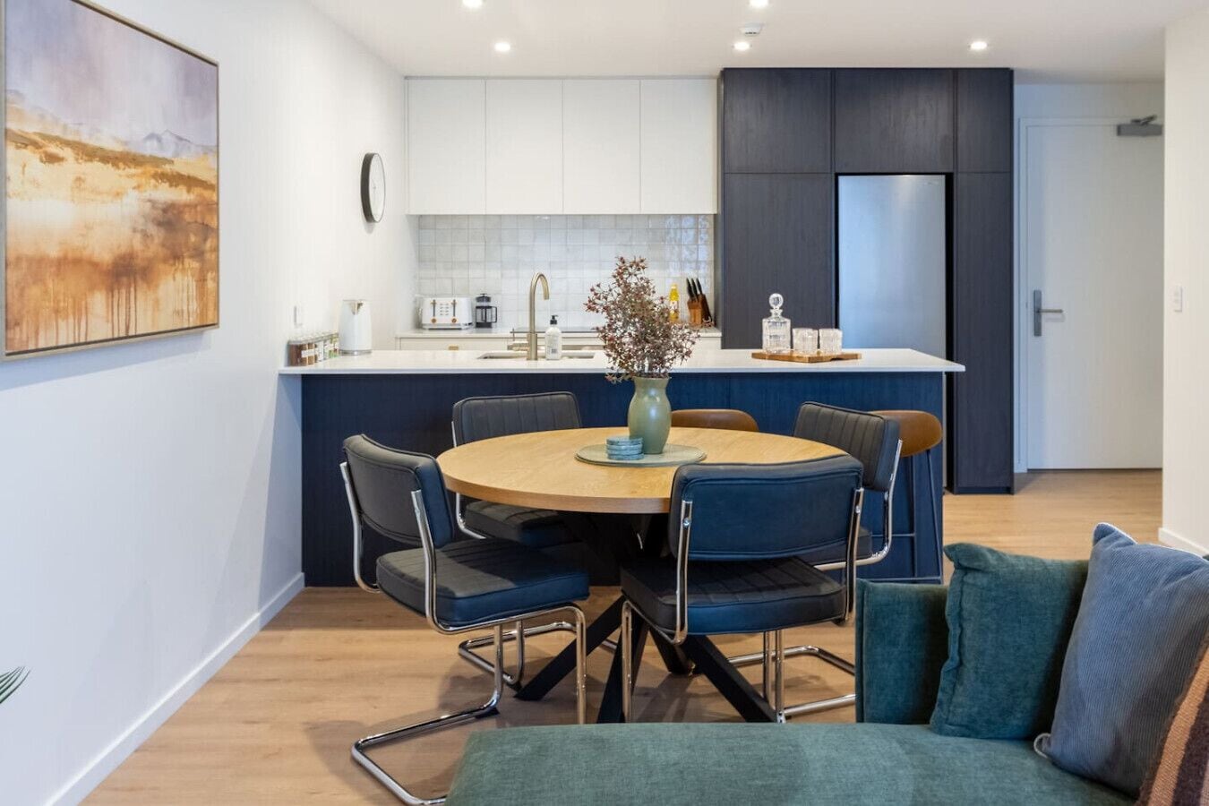A modern kitchen with white cabinets, a central island, and a dining area with a round table and chairs.