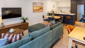 Una sala de estar moderna con un sofá, una mesa de centro y un televisor. Hay un comedor con una mesa y sillas.