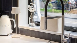 A modern kitchen with a stainless steel sink, a kettle, and a vase with flowers on the windowsill. - Executive Accommodation. 3 Bed, 3 bath + Garage (Christchurch)