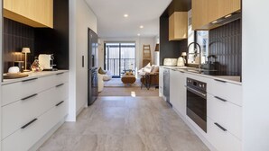 A modern kitchen with white cabinetry, a central island, and a dining area with a sofa and table. - Executive Accommodation. 3 Bed, 3 bath + Garage (Christchurch)