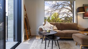 A modern living room with a brown sofa, a round black table, and a white rug. - Executive Accommodation. 3 Bed, 3 bath + Garage (Christchurch)