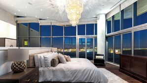 Une chambre moderne avec un grand lit, une table de chevet, une commode et une vue sur la ville la nuit.
