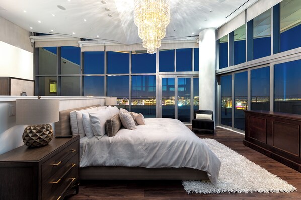 Ein modernes Schlafzimmer mit einem großen Bett, einem Nachttisch, einer Kommode und Blick auf die beleuchtete Stadt.