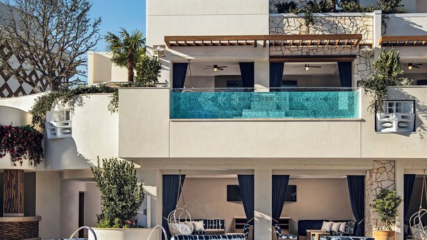 Un hôtel moderne doté d’une piscine sur le toit, de palmiers et d’une façade en pierre.