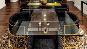 Un comedor moderno con una mesa de vidrio, sillas tapizadas en negro y una pieza decorativa dorada en el centro.