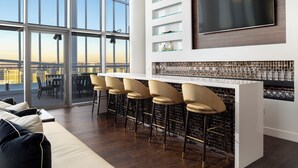 Un espace bar moderne doté d’un grand téléviseur, de verres à vin et offrant une vue sur la ville.