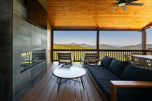 A wooden deck with a sofa, chairs, and a table, overlooking a mountainous landscape.