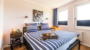 Une chambre à coucher bien rangée, avec un lit, une table de chevet sur laquelle se trouve une lampe, une petite horloge et un objet décoratif accroché au mur.
